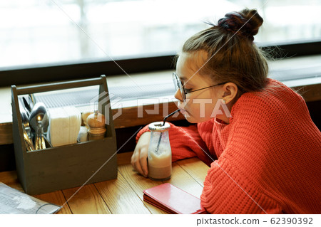 Girl teenager sitting in a cafe at a table waiting and drinking  62390392