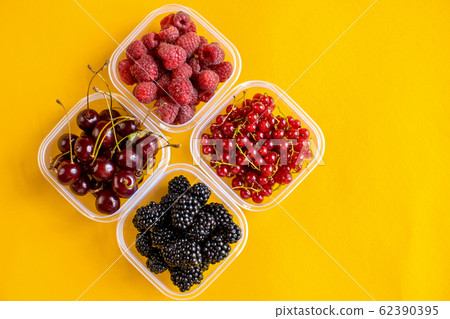 4 plastic plates, containers with raspberry, blackberry, red currant, cherry on a yellow background 62390395