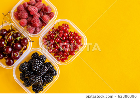 4 plastic plates, containers with raspberry, blackberry, red currant, cherry on a yellow background 4 plastic plates, containers with raspberry, blackberry, red currant, cherry on a yellow background 62390396