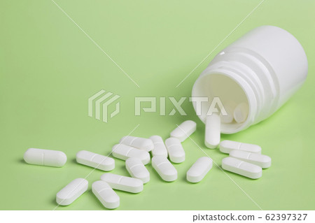 Plastic white bottles of pills on a green background of scattered white pills Plastic white bottles of pills on a green background of scattered white pills 62397327
