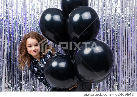 Attractive young girl holds with airy black helium balloons on a brilliant festive background 62409648