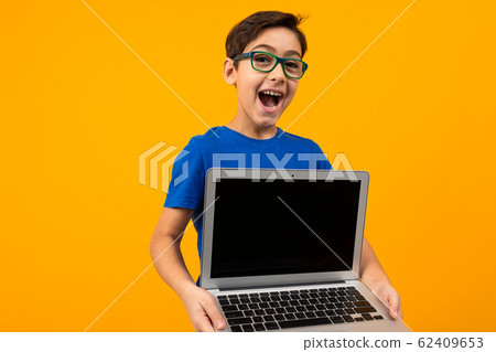 joyful caucasian boy holds laptop screen forward with mock up on yellow studio background with copy 62409653