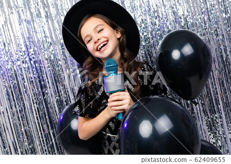 fashionable young girl sings in karaoke at a party with a microphone in her hands on a shiny 62409655