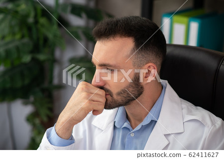 Dark-haired bearded doctor in a white robe looking stressed 62411627