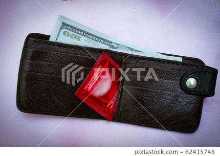 Closeup woman hand holding black Leather Wallet with a red condom at the black background 62415748