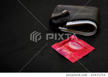 Closeup woman hand holding black Leather Wallet with a red condom at the black background 62415754