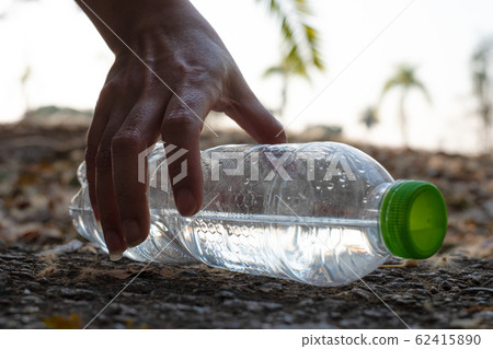 Close up Hand picking up clear plastic bottle water drink with a green cap on the road in the park at blurred background 62415890