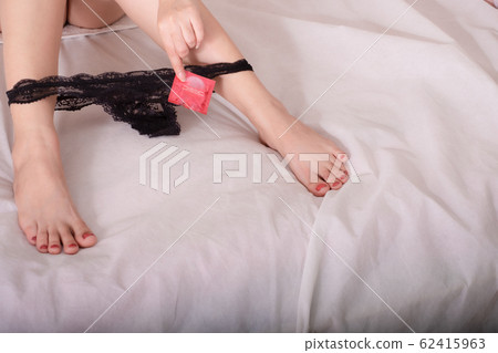 Beautiful leg sexy woman hand holding condom and reclines on the bed with black g-string between feet Beautiful leg sexy woman hand holding condom and reclines on the bed with black g-string between feet 62415963