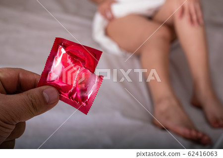 Man showing red condom at the beautiful woman with towel lies in bed, Safe sex and health care and medical 62416063