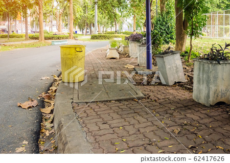An old yellow dustbin in the public park beside the walk way for protect environment. An old yellow dustbin in the public park beside the walk way for protect environment. 62417626