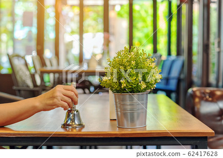 The female client's right hand hold a small bell to shake for call the waiter in coffee shop. The female client's right hand hold a small bell to shake for call the waiter in coffee shop. 62417628
