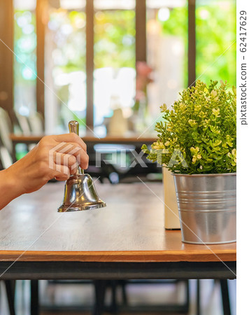 The female client's right hand hold a small bell to shake for call the waiter in coffee shop. The female client's right hand hold a small bell to shake for call the waiter in coffee shop. 62417629
