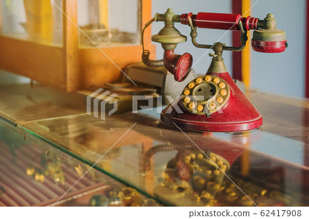 A red telehones with rotary dial with dust and scratches and credit card machine in ancient times placed on a glass showcase in an old gold shop in Asia. A red telehones with rotary dial with dust and scratches and credit card machine in ancient times placed on a glass showcase in an old gold shop in Asia. 62417908
