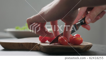closeup man cut cherry tomatoes in halves on olive board closeup man cut cherry tomatoes in halves on olive board 62418255
