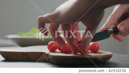 closeup man cut cherry tomatoes in halves on olive board closeup man cut cherry tomatoes in halves on olive board 62418256