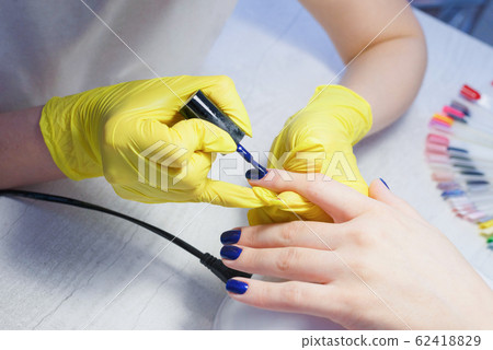Applying a colors nail polish by a qualified master in a beauty salon. 62418829