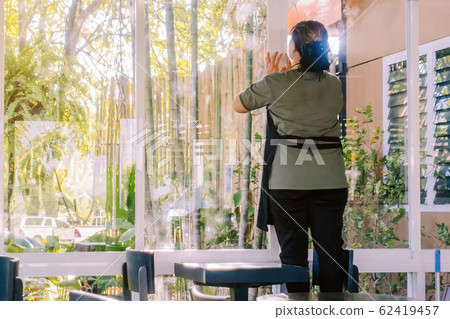 Back view of maid closes the glass window to turn on the air conditioner in the coffee shop. Back view of maid closes the glass window to turn on the air conditioner in the coffee shop. 62419457