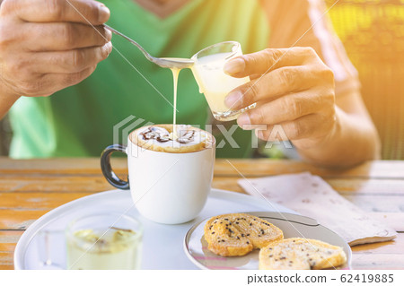 A man pour milk into a coffee cup using a spoon to prevent excess sweetness and eaten with biscuits paired with Chinese tea for an afternoon snack. A man pour milk into a coffee cup using a spoon to prevent excess sweetness and eaten with biscuits paired with Chinese tea for an afternoon snack. 62419885