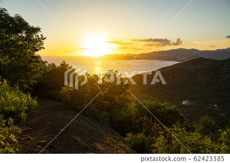 Bright sun rising over calm sea surrounded by hills 62423385
