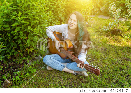 Young hipster woman sitting in grass and playing 62424147