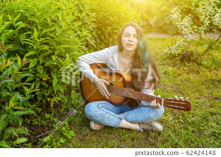 Young hipster woman sitting in grass and playing 62424148