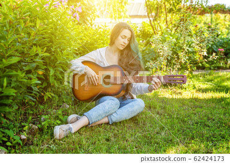 Young hipster woman sitting in grass and playing Young hipster woman sitting in grass and playing 62424173
