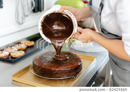 Patissier pouring liquid chocolate on a cake 62425884