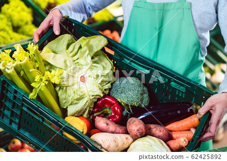 Woman working in organic supermarket putting veggies in a box 62425892