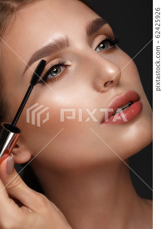 Beautiful girl with sexy lips and classic makeup with cosmetic mascara brush in hand. Beauty face. Beautiful girl with sexy lips and classic makeup with cosmetic mascara brush in hand. Beauty face. 62425926