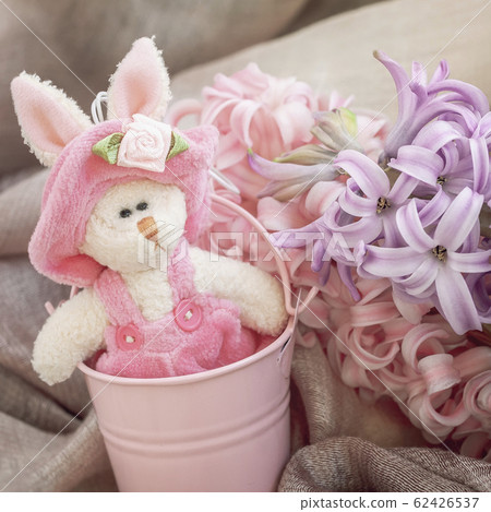 Easter bunnie in pink little bucket, next to a spring flowers. Home holiday composition 62426537