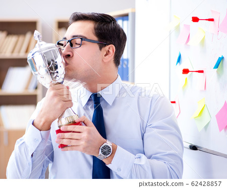 Young businessman receiving prize cup in office Young businessman receiving prize cup in office 62428857