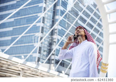 Handsome modern Arabian man using holding smart tablet. Arab Man use smartphone calling walking city Handsome modern Arabian man using holding smart tablet. Arab Man use smartphone calling walking city 62431360