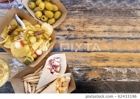 Tapas, pinchos, and wine, shot from above on a wooden table. Cheese, jamon and olives, spicy gildas and potato chips in a street cafe with copy space Tapas, pinchos, and wine, shot from above on a wooden table. Cheese, jamon and olives, spicy gildas and potato chips in a street cafe with copy space 62433196