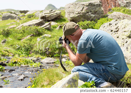 Hiker with camera taking picture of small stream 62440157