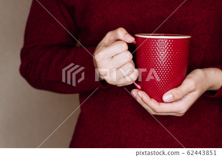 Young woman in red sweater is holding red cup of tea or coffee Young woman in red sweater is holding red cup of tea or coffee 62443851
