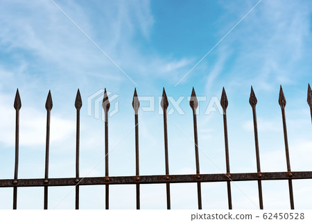 Wrought iron fence with sharp points on blue sky with clouds Wrought iron fence with sharp points on blue sky with clouds 62450528