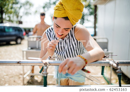 Young woman at summer festival, brushing teeth by basins. 62453163