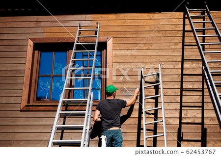 A mature man outdoors in summer, painting wooden house. 62453767