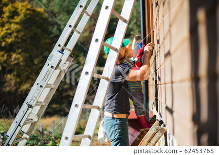 A father and toddler boy outdoors in summer, painting wooden house. 62453768