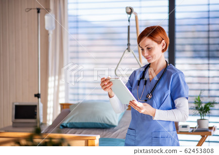 Portrait of female doctor or nurse standing in hospital room, using tablet. 62453808