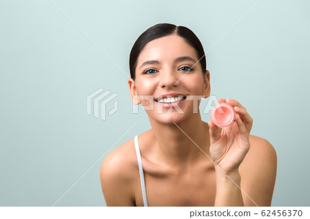 cheerful beauty woman with blue eyes holding a small jar of cream on blue background. seasonal skin protection 62456370
