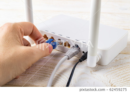 Woman hand plugging a blue network cable into socket of a white Wi-Fi wireless router. Woman hand plugging a blue network cable into socket of a white Wi-Fi wireless router. 62459275