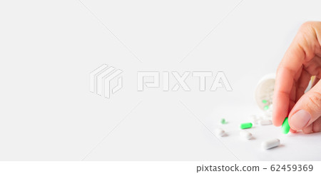 Palm hand with green one from other white scattering pills. Woman gripes hand with capsules with medicines on light background with copy space. 62459369