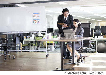 A man who looks at a woman using a computer in the office 62468824