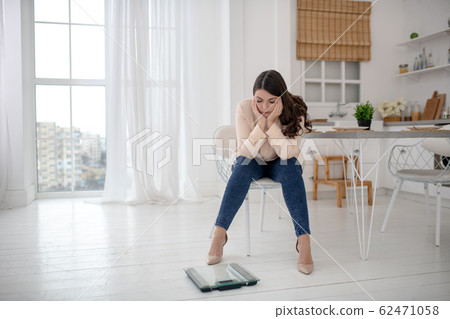 Young woman in a beige blouse sitting and feeling upset 62471058