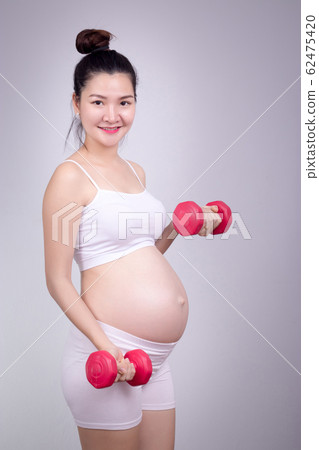 Pregnant exercises concept.A portrait of a Beautiful asian pregnant woman doing light exersice by using dumbell at home. Pregnant exercises concept.A portrait of a Beautiful asian pregnant woman doing light exersice by using dumbell at home. 62475420