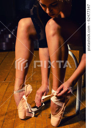 elegant ballet dancer tying her pointe shoes 62477347