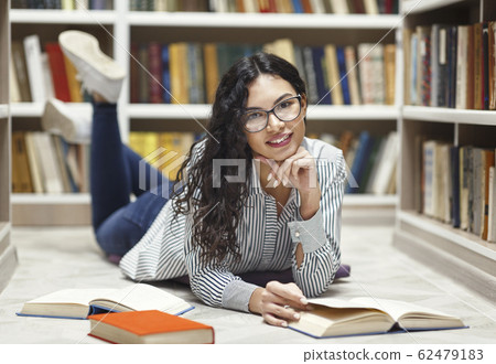 Smiling latina girl reading books lying at library Smiling latina girl reading books lying at library 62479183