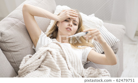 Sick young woman checking her temperature at home 62479751