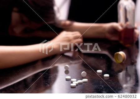 a drug addict not conscious on the table with several pill spilled on table near bottle of alcohol. 62480032